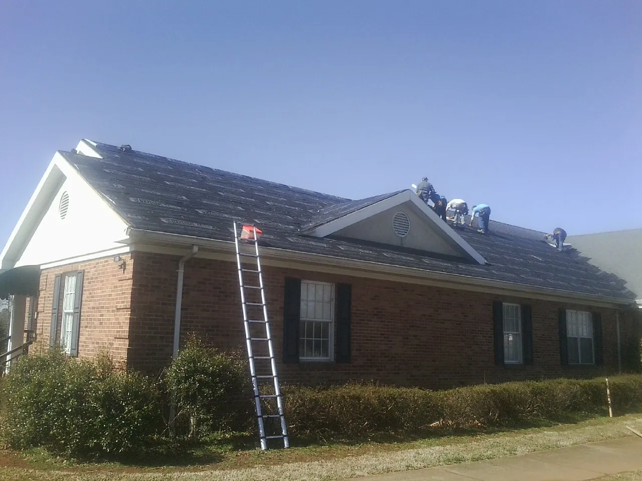 Crew tearing shingles off a brick ranch roof with a ladder set — Emergency Roof Repair work by our crew in Escondido