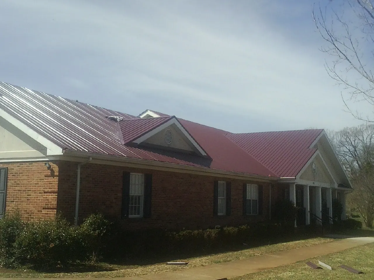 Red metal roof with gabled entries on a long brick building, from a Hail Damage Roof Repair job in Escondido