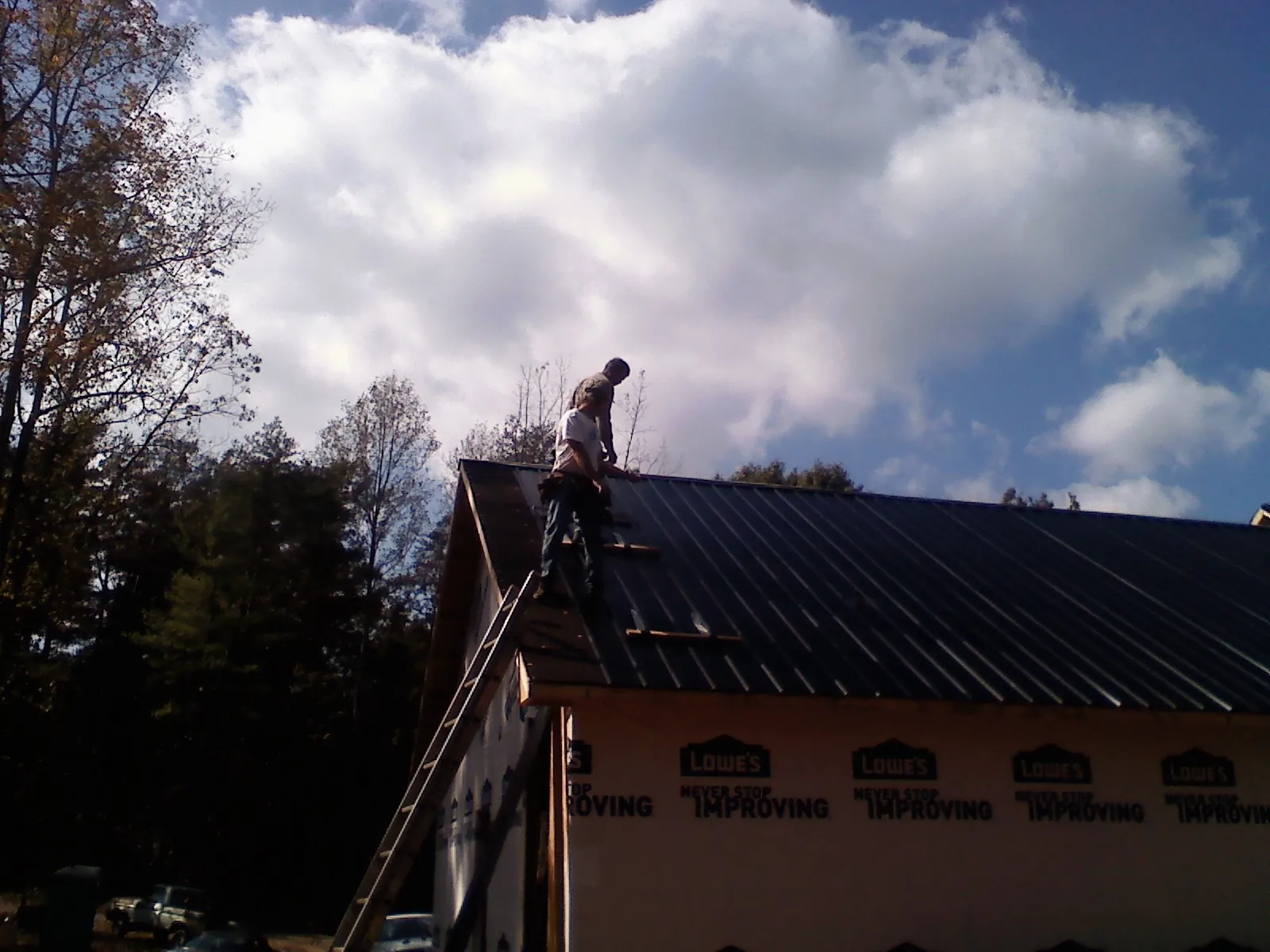 Roofer fastening dark metal panels high against a cloudy sky, from a Roof Inspection job in Escondido