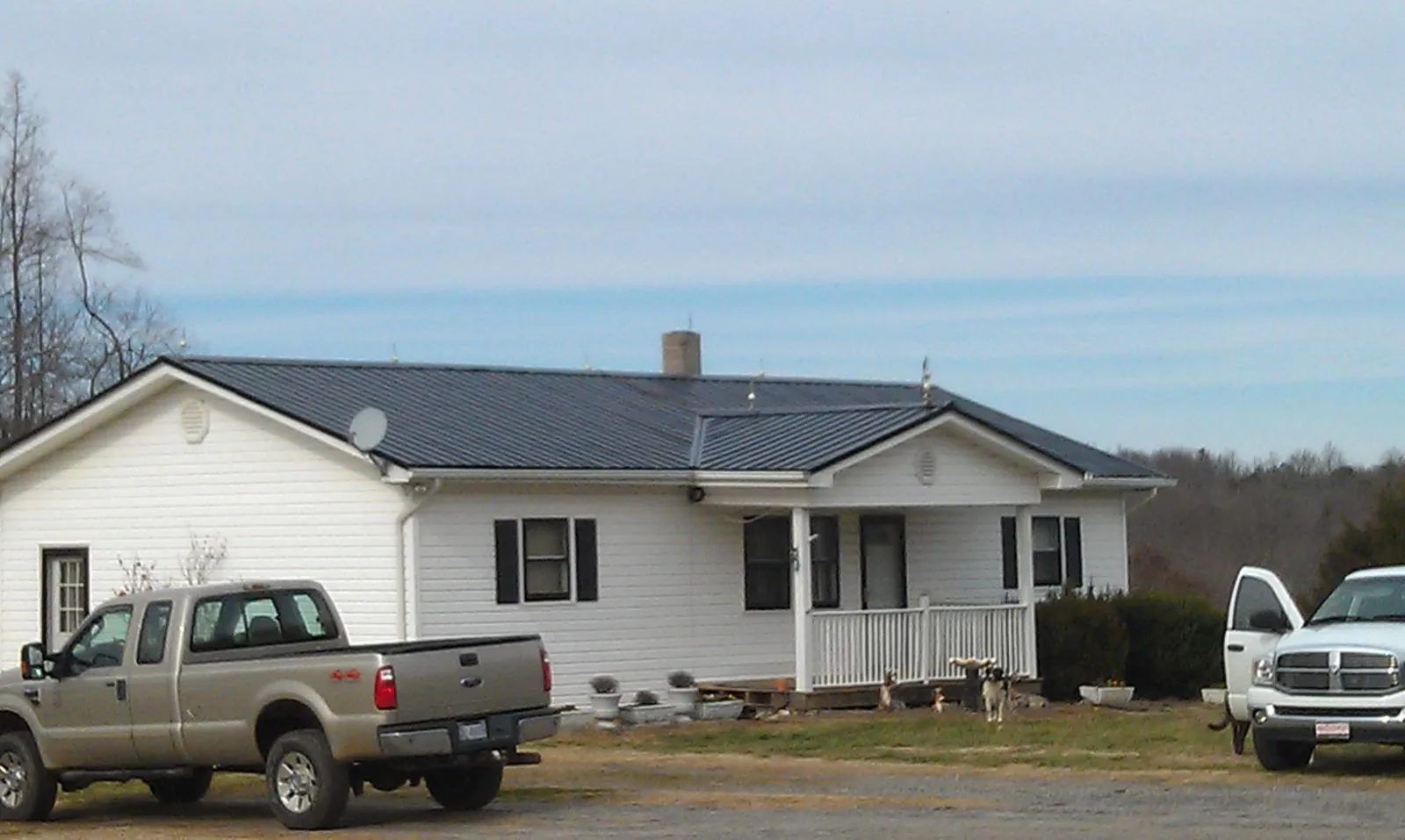 Finished dark metal roof on a white ranch home with work trucks parked in Escondido